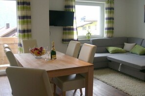 Ein Wohnzimmer mit einem Holzesstisch, einem grauen Sofa und einem an der Wand befestigten Fernseher.