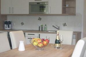 Eine Küche mit Esstisch, Obstschale, einer Champagnerflasche und einer Kaffeemaschine.