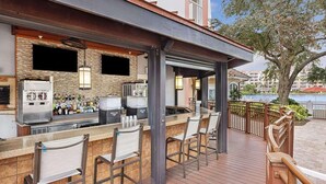 An outdoor bar area with a poolside view, featuring a bar counter, seating, and a view of a body of water.