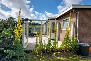 Ein Haus mit Wintergarten, Backsteinfassade und einem Garten mit gelben Blumen.