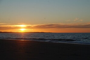 Ein Strand bei Sonnenuntergang, die Sonne versinkt am Horizont.