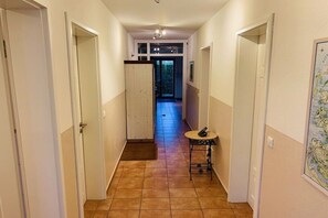Ein Korridor mit Fliesenboden, einem kleinen runden Tisch und einem Stuhl, sowie einer Tür zu einem weiteren Zimmer.