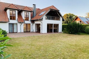 Ein zweigeschossiges Haus mit geneigtem Dach, großen Fenstern und einer überdachten Terrasse.