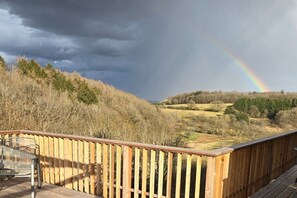 Eine Holzterrasse mit einem Metallstuhl, mit Blick auf eine Landschaft mit einem Regenbogen.