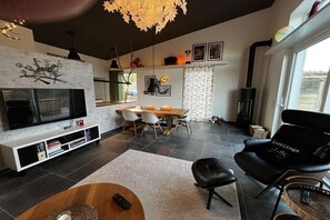 Ein modernes Wohnzimmer mit Flachbildfernseher, Kamin, Essbereich mit Stühlen und einem großen Fenster.