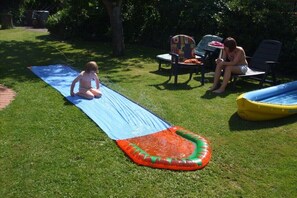 Une zone herbeuse avec un toboggan gonflable bleu et une piscine gonflable jaune.