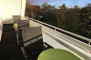 Ein Balkon mit Gartenmöbeln, einem weißen Geländer und Blick auf Bäume sowie ein Haus im Hintergrund.