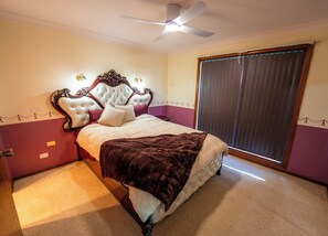 A bedroom with a large bed, a ceiling fan, a window with blinds, and a carpeted floor. - Sanctuary Family Escape | Pet-Friendly Getaway Near Jervis Bay (Sanctuary Point)