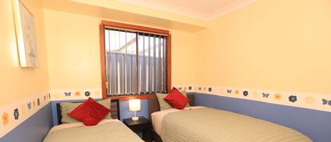 A bedroom with two beds, a window with blinds, and a decorative border on the walls.