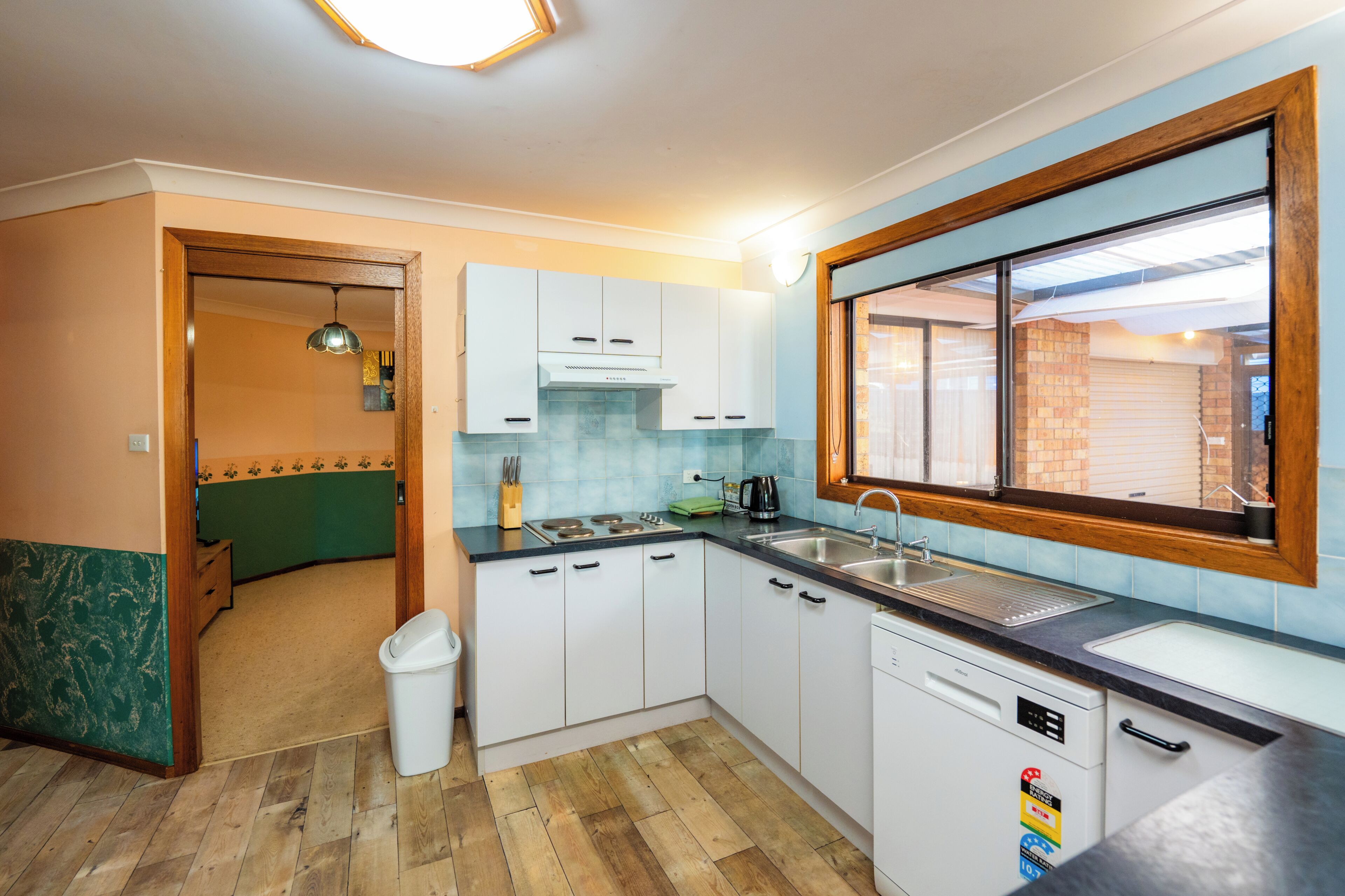 A kitchen with white cabinets, a dishwasher, a window, and a wooden floor.