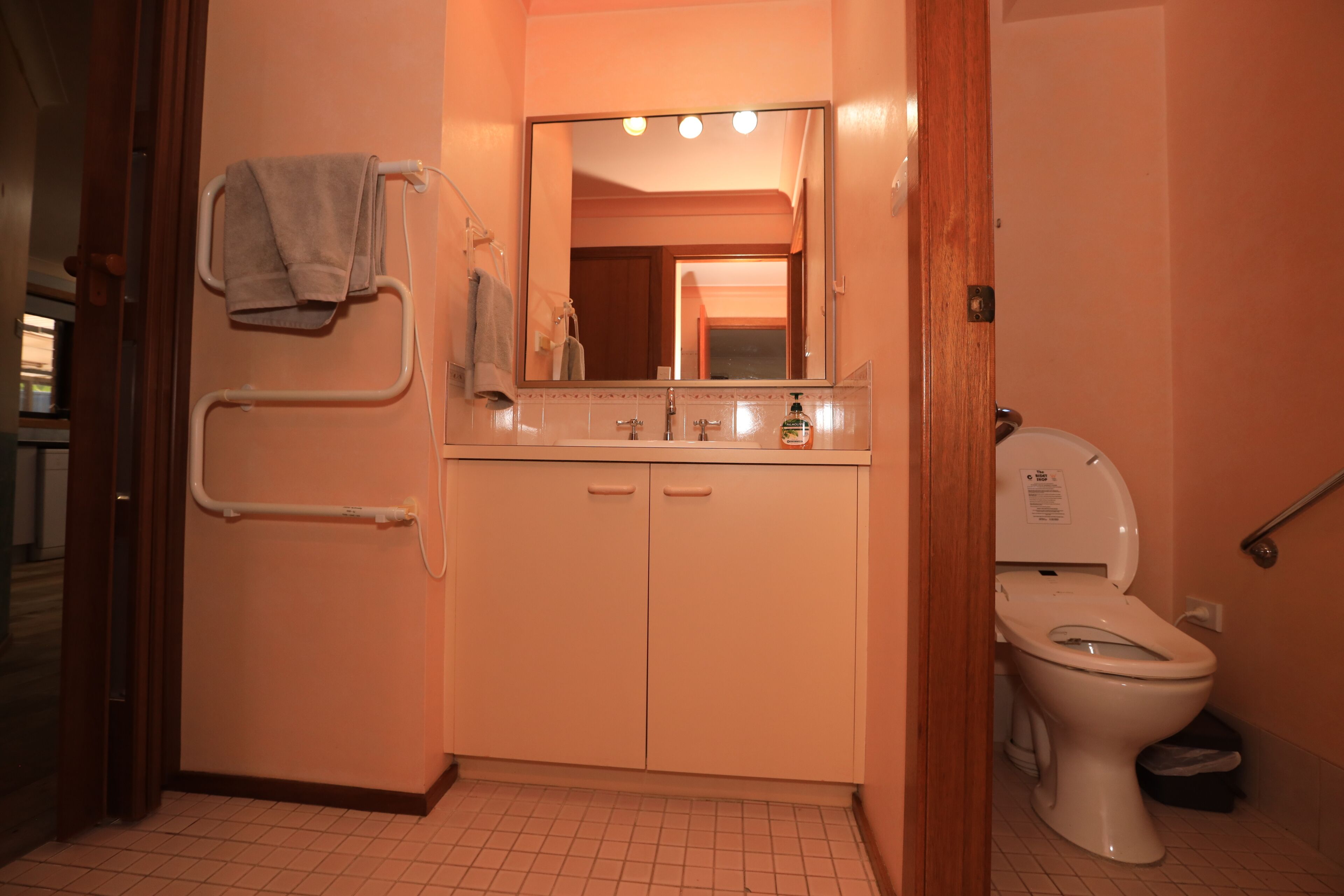 A bathroom with a toilet, sink, mirror, towel rack, and grab bar.