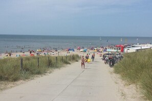 Ein Strand mit einem Betonweg, der zum Wasser führt, Sonnenschirmen und badenden Gästen.