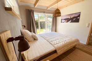 Ein Schlafzimmer mit einem Bett, einer Hängelampe, einem Fenster mit Vorhängen und einem Bild an der Wand.