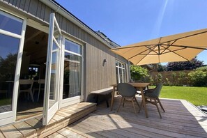 Eine offene Terrasse mit Tisch und Stühlen, einem großen Sonnenschirm und einer Schiebetür zu einem Innenbereich.