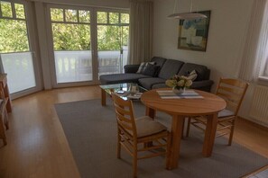 Una sala de estar con un sofá, una mesa redonda de madera con sillas, una mesa de centro de vidrio y un cuadro en la pared.