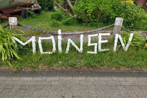 Una cerca de madera blanca con la palabra 'MOINES' pintada, rodeada de follaje.