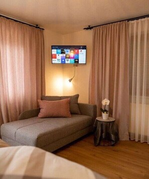Ein Zimmer mit einer Couch, einem kleinen Tisch mit einer Blume und einem an der Wand befestigten Fernseher.