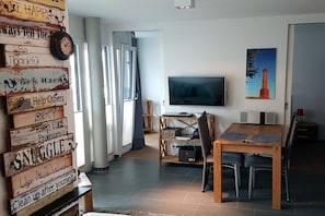 A modern living room with a TV, wooden dining table, and a motivational sign with various phrases. - Schippers Huus No. 1 (Norderney)