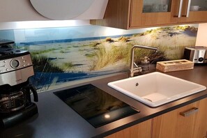 A kitchen with a modern stove, a sink, and a backsplash with a beach scene. - Schippers Huus No. 1 (Norderney)