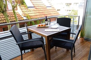 A balcony with a wooden table, two black chairs, a bottle of wine, and a plate with fruit. - Schippers Huus No. 1 (Norderney)
