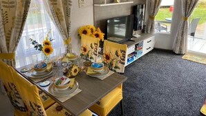 A compact living space with a dining area, a television, and a small kitchen area. - Sunflower Lodge Luxury Pet Free Holiday Caravan (Filey)