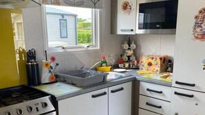 A kitchen with white cabinets, a stove, a microwave, and a window with a view of a house. - Sunflower Lodge Luxury Pet Free Holiday Caravan (Filey)
