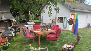 An outdoor patio with a wooden table, red chairs, and a barbecue grill. - That ’70s Tent • Flower Power • Mt. Rainier & Salish Sea Views (Vashon)