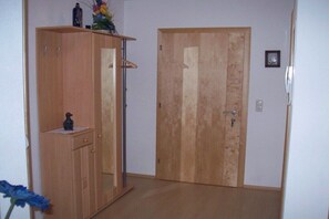 Ein Zimmer mit einem Holzschrank, einem kleinen Tisch mit einer Vase und einer Tür.