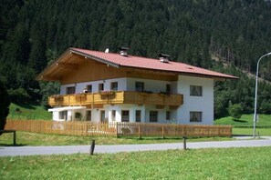 Eine zweistöckige Chalet mit rotem Ziegeldach, Holzbalkonen und einer weißen Fassade.