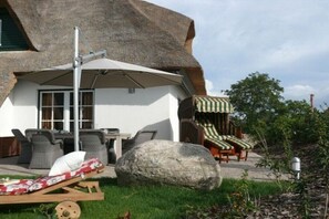 Ein Gebäude mit einem Strohdach, Sitzgelegenheiten im Freien, einem Tisch und einem großen Felsen.