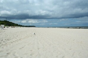 Ein Strand mit sandigem Ufer, einem Steg und einem Leuchtturm in der Ferne.