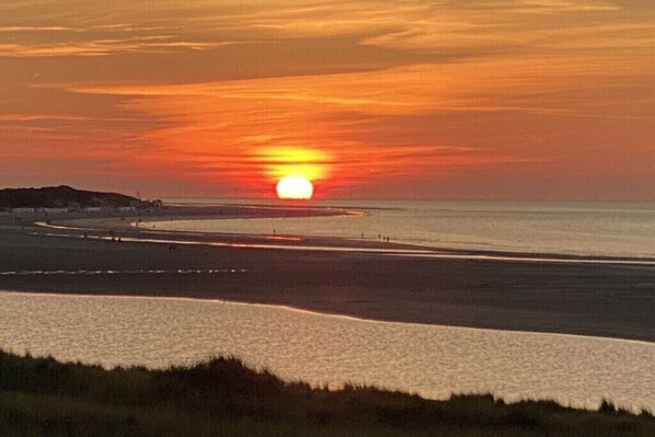 A sunset over a coastal area with a beach and a road curving along the shore. - Zomprus holiday home (Kamperland)