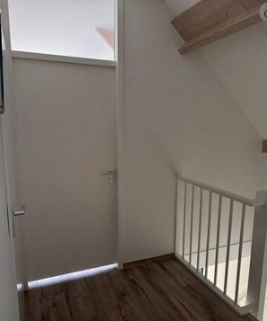 A room with a wooden floor, white walls, a white door, and a white railing. - Zomprus holiday home (Kamperland)