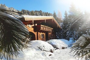 A wooden cabin with a covered porch, surrounded by snow-covered ground and pine trees. - Zirbenchalet Eggriedl (Großarl)