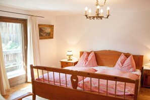 A bedroom with a wooden bed, a nightstand with a lamp, a chandelier, a window with curtains, and a painting on the wall. - Holiday home in Uttendorf with Wi-Fi (Uttendorf)