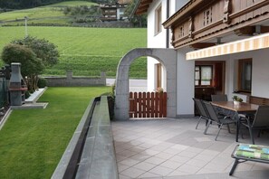 Eine Terrasse mit Tisch und Stühlen, ein steinerner Bogen und Blick auf einen grünen Hügel.