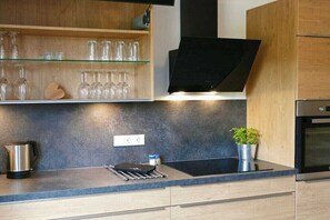 Eine moderne Küche mit Holdekor, einer schwarzen Dunstabzugshaube, einem Glasregal mit Weingläsern, einem Wasserkocher und einem Topf mit Pflanze.