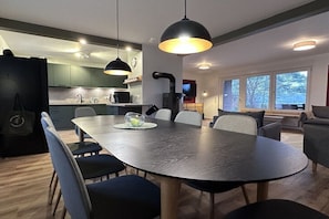 Eine moderne Küche mit Essbereich, inklusive großem Tisch und Stühlen, Pendelleuchten und Blick ins Freie.