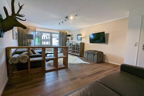 A living room with a sofa, a wooden bench, a television mounted on the wall, and a large window. - Holiday apartment with 2 bedrooms (Chieming)