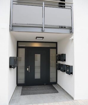 A modern building entrance with a dark-colored door, a small overhang, and two wall-mounted intercoms. - Holiday apartment with 2 bedrooms (Chieming)