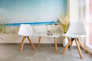 A room with a beach mural, two white chairs, a small round table, and a vase with plants. - Holiday home with 4 bedrooms (18445 Kramerhof, Deutschland OT Parow)
