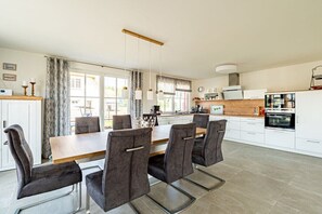 A modern kitchen with a dining area, featuring a wooden table and chairs, a built-in oven, and a large window. - Holiday home with 4 bedrooms (18445 Kramerhof, Deutschland OT Parow)