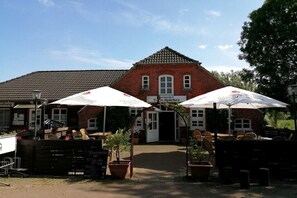 A brick building with a sign reading 'Tisch Specker' and outdoor seating with umbrellas. - Hansmeier in the Eckwarderhörne holiday village (Butjadingen)