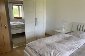 Ein Schlafzimmer mit einem Bett, einem Schrank, einem Nachttisch mit Lampe und einem Fenster mit Vorhängen.