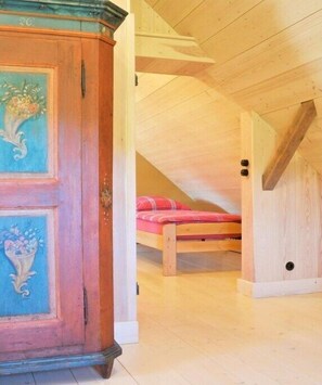 Ein Zimmer mit einem hölzernen Bett, einem Schrank mit floralem Dekor und einer geneigten Decke.