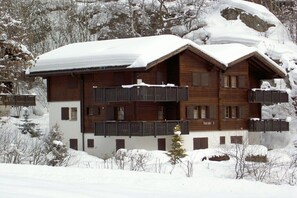 Ein mehrstöckiges Holzhaus mit Balkonen, umgeben von schneebedeckten Bäumen und Hügeln.