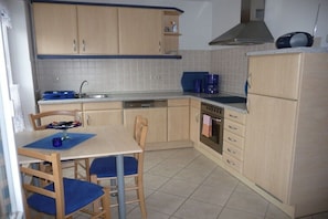 A compact kitchen with wooden cabinets, a dishwasher, a stove, and a coffee maker. - Holiday apartment in Waren with Wi-Fi (Waren)