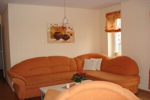 A living room with an orange sofa, a white coffee table, and a painting on the wall. - Holiday apartment in Waren with Wi-Fi (Waren)