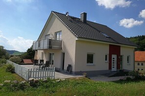 Ein zweistöckiges Haus mit Balkon, rotem Eingang und kleinem Garten.