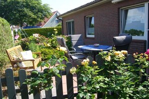 Eine Terrasse mit Sitzgelegenheiten, ein Backsteinhaus und ein Hecken.